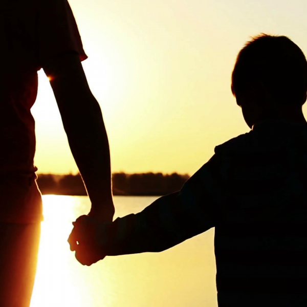 Father holding sons hand, water and sunset